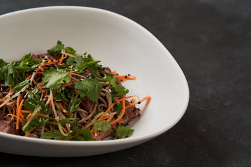Thai style warm soba salad in white bowl on gray table background