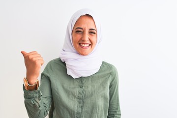 Young beautiful Arab woman wearing traditional Muslim hijab over isolated background smiling with happy face looking and pointing to the side with thumb up.