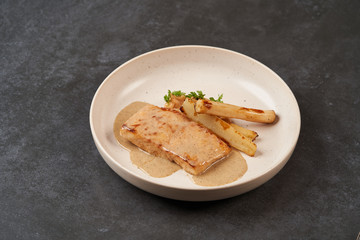 Baked Sturgeon fillet with spinach on a white plate on gray table