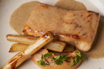 Baked Sturgeon fillet with spinach on a white plate on gray table