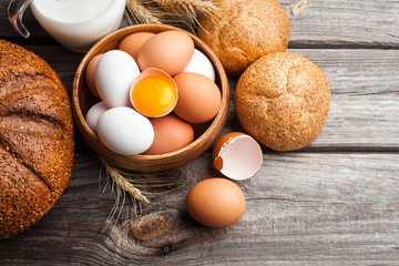 Raw broken egg with yolk in a wooden bowl. Fresh white and brown chicken eggs on wooden background