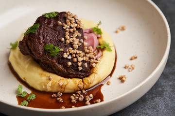 Stewed veal cheeks with mashed potatoes on a white plate, close-up.