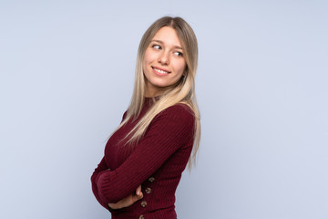 Young blonde woman over isolated blue background with arms crossed and happy
