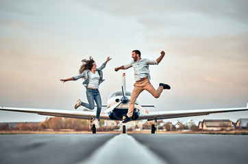 Playful couple jumping and smiling on the airport - obrazy, fototapety, plakaty