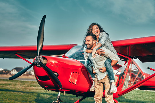 Happy Young Couple Laughing And Having Fun On Runway Near Private Aircraft