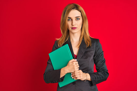 Young beautiful redhead businesswoman wearing suit holding book
