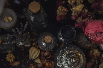 vintage jars, bottles, containers, flowers in smoke and dry leaves on a wooden table with warm light
