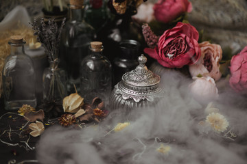 vintage jars, bottles, containers, flowers in smoke and dry leaves on a wooden table with warm light