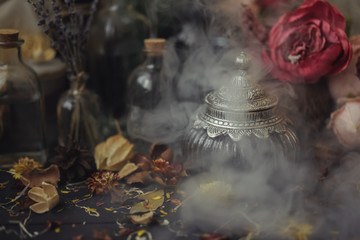 vintage jars, bottles, containers, flowers in smoke and dry leaves on a wooden table with warm light