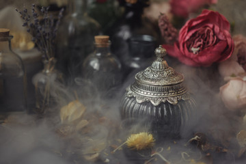 vintage jars, bottles, containers, flowers in smoke and dry leaves on a wooden table with warm light
