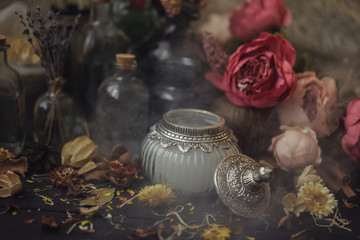 vintage jars, bottles, containers, flowers in smoke and dry leaves on a wooden table with warm light