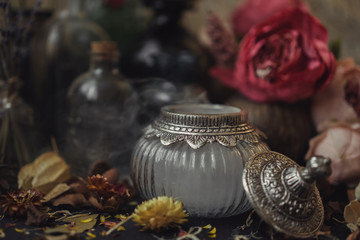 vintage jars, bottles, containers, flowers in smoke and dry leaves on a wooden table with warm light