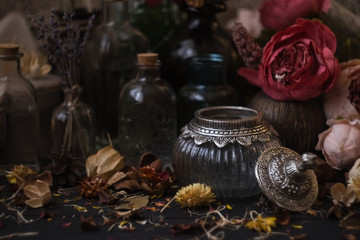 vintage jars, bottles, containers, flowers in smoke and dry leaves on a wooden table with warm light