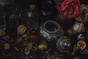 vintage jars, bottles, containers, flowers in smoke and dry leaves on a wooden table with warm light