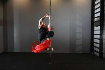The dancer on the pylon in the studio. Girl doing exercises on a sports equipment.