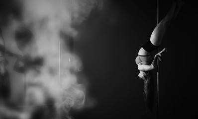 The dancer on the pylon in the studio. Girl doing exercises on a sports equipment.