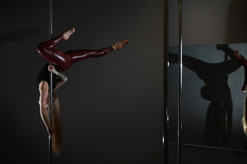 The dancer on the pylon in the studio. Girl doing exercises on a sports equipment.