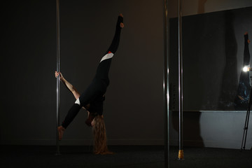 The dancer on the pylon in the studio. Girl doing exercises on a sports equipment.