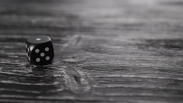 Black dice spins and rolls on a dark wooden texture table. Stops with the number 1 on top. The idea of bankruptcy and unsuccessful business and gambling. Slow motion