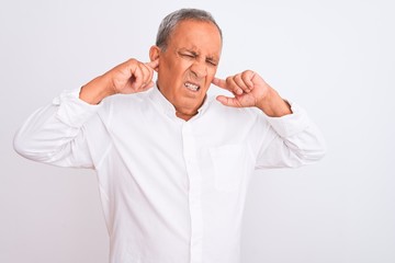 Senior grey-haired man wearing elegant shirt standing over isolated white background covering ears with fingers with annoyed expression for the noise of loud music. Deaf concept.