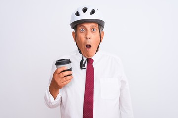Senior businessman wearing bike helmet drinking coffee over isolated white background scared in shock with a surprise face, afraid and excited with fear expression
