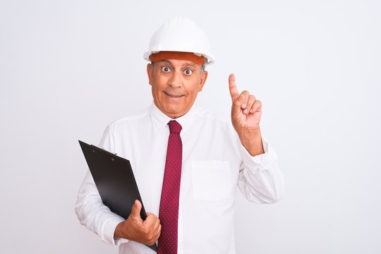 Senior architect man wearing security helmet holding clipboard over isolated white background surprised with an idea or question pointing finger with happy face, number one