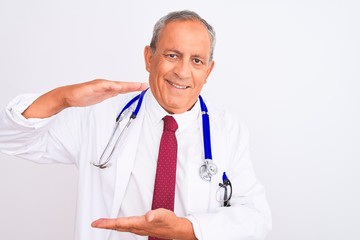 Senior grey-haired doctor man wearing stethoscope standing over isolated white background gesturing with hands showing big and large size sign, measure symbol. Smiling looking at the camera. Measuring