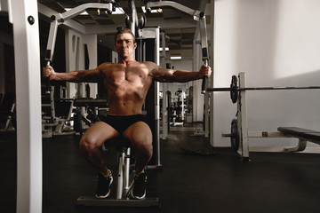 Fototapeta premium Portrait of fitness athlete man with muscular body does exercises on sports equipment in the gym, workout arm muscles, pumping biceps and triceps