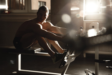 Portrait of fitness athlete man with muscular body does exercises on sports equipment in the gym,...