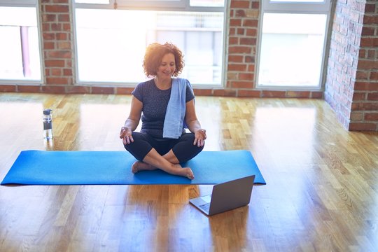 Middle age beautiful sportswoman smilig happy. Sitting on mat with smile on face using laptop at home