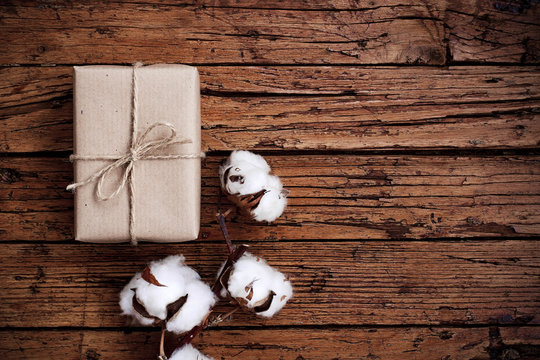 Gift box and cotton flowers on wooden background. Present wrapped in brown kraft paper. Decoration in rustic style. Concept of zero waste and plastic free. Flat layout. Copy space.