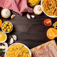 Fototapeta na wymiar Italian food ingredients with pasta, vegetables, mushrooms, olives and bacon. Flat lay of mediterranean cuisine ingredients on dark wooden background, copy space