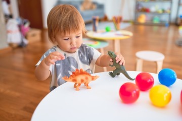 Adorable toddler playing with dinosaurs around lots of toys at kindergarten