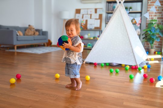 Adorable toddler playing with balls around lots of toys at kindergarten