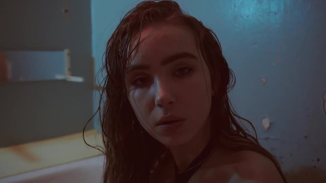 Close up of young woman taking shower in slow motion. Closeup wet woman washing hair in bathroom in red light. Provocative woman touching wet hair in washroom.