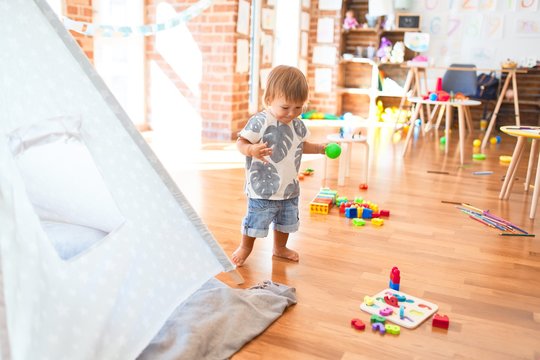 Adorable toddler playing around lots of toys at kindergarten