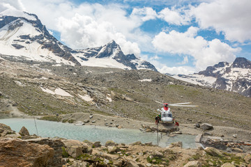 Fototapeta premium Rescue helicopter landing near mountain lake providing assistance.