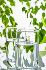 Two glasses of water on a green natural background. There's a splash of water in the glass.