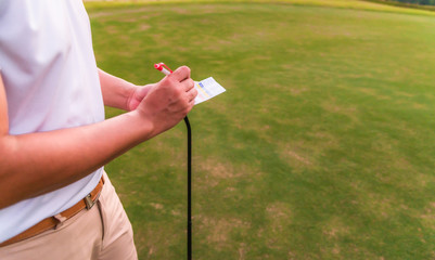 Asian male golfer using pen writing his golf score on scorecard