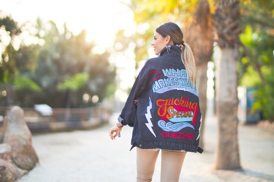 Young beautiful woman wearing denim jacket standing backwards at the town park
