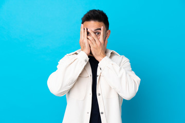 Young handsome man over isolated blue background covering eyes and looking through fingers