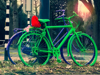 Fototapeta na wymiar Two painted multi-colored bicycles with a soft toy heart, winter outdoors in the evening. Romantic Valentine day, concept.