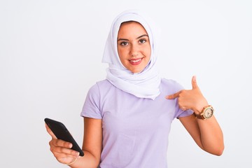 Young beautiful arabian girl wearing hijab using smartphone over isolated white background with surprise face pointing finger to himself