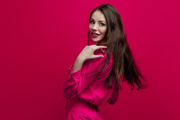 Obraz premium Cute and cheerful young brunette in a pink suit on a pink background