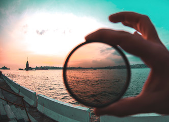 a man holding a photo filter with backgorund of Maiden Tower during sunset