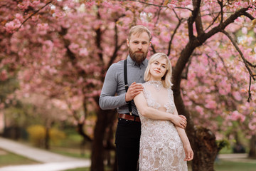 Fototapeta premium portrait of young beautiful couple in blossoming pink cherry blossom, sakura garden and hugging on a sunny day. Spring wedding portrait. valentine's day.