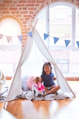 Beautiful toddler girl sitting on the floor playing with unicorn and doll inside  tipi at...
