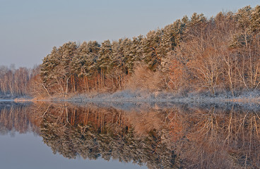 Winter landscape of the frosted shoreline of Crooked Lake at sunrise with mirrored reflections in...