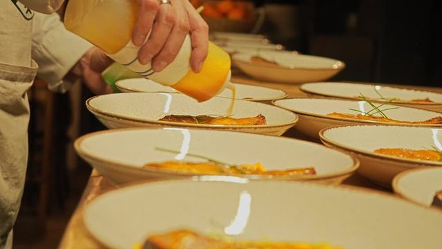 The chef puts food on plates. Pours yellow sauce on fish or meat. Club, restaurant. Yellow sauce is poured on a salmon in a faience plate.