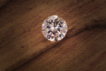 A colorless round cut diamond sits on a sandstone background.